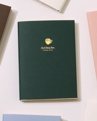 Green notebook with a gold logo of a coffee on a white surface, reads "Tea & Diary Time"