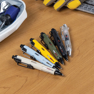 Six retractable multi-tool pens in assorted colors (white, light blue, yellow, olive green, black, and clear) arranged on a wooden desk next to a zippered case and tools.