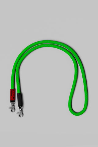 A bright green bag rope strap with silver metal snap hooks and a black handle on a solid gray background.