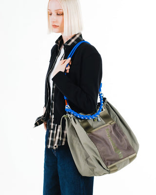Person wears olive green bag with a blue braided shoulder strap