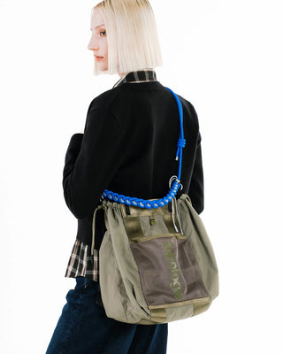 Person carrying a large olive green bag with a bright blue braided strap
