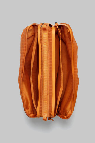 An orange zippered pouch with a grid-patterned fabric exterior and matching orange webbing straps, shown from a top-down view on a solid gray background.