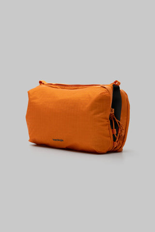 Side angle view of orange grid sacoche bag against a light gray background