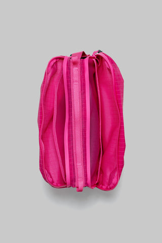 A bright pink nylon bag with a vertical zipper closure, shown from a top-down view on a neutral gray background.