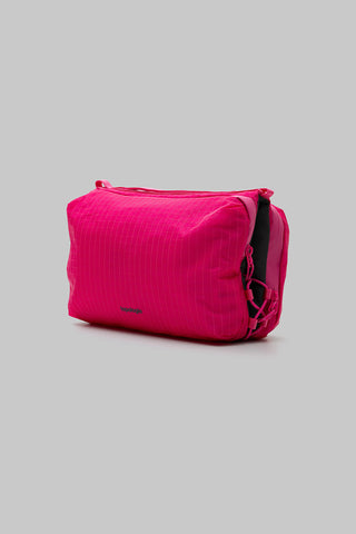 A bright pink bag with a subtle vertical texture, shown from a three-quarters angle on a solid gray background.