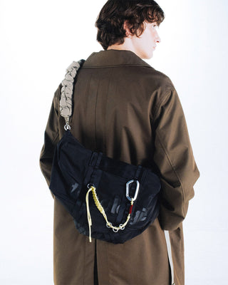 Person wearing a black bag over one shoulder with keychain attatched on a white background