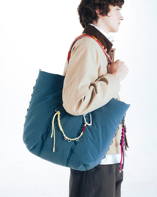 Person wearing large blue bag on their shoulder with yellow keychain attatched