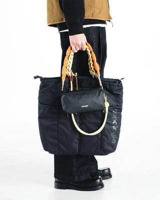 Black helmet bag held by person with front panels, handle loop, and side details