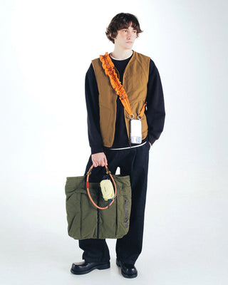 Olive helmet bag carried by person, with shoulder straps and front pocket