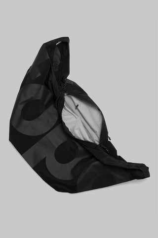 A black nylon bag with large branding letters shown open to a light gray interior lining, set against a solid gray background.