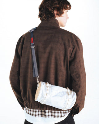 White utility sling bag worn across back with teal strap and metal clip
