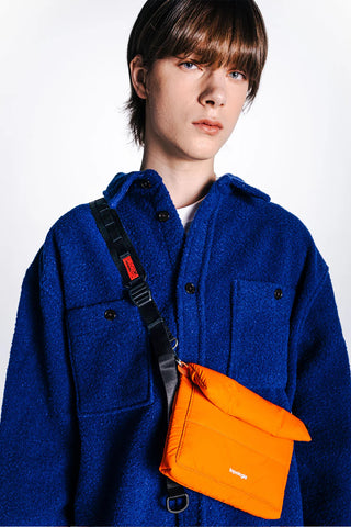Orange utility sling bag with black strap and red accent label