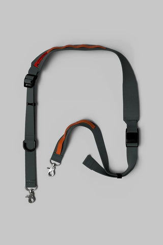 Dark gray and orange wide bag strap with clips and hardware on a gray background