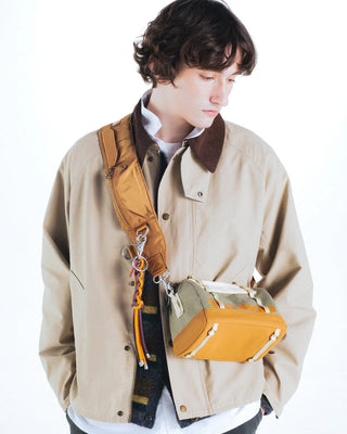 Person wearing a beige jacket with an orange bag over their shoulder with a keychain attached