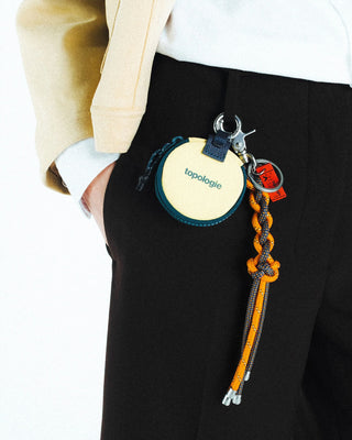 Keychain with a circular bag and braided rope attached to a person's pants.