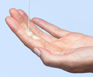 Hand with a small amount of liquid cream on a light blue background