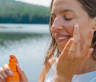 Woman applying face serum with a scenic lake background