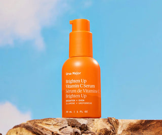 Orange serum bottle labeled 'UrsaMajor Brighten Up Vitamin C Serum' against a blue sky background.