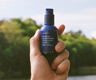 Hand holding a bottle of Ursa Major Fortifying Gel Moisturizer with a blurred natural background
