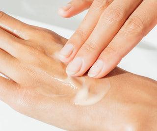 Hand applying cream to another hand on a light background