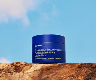 Blue jar of Ursa Major Golden Hour Recovery Cream on a wooden surface with a blue sky background