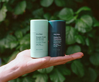 Two deodorant bottles held in a hand with a green leafy background