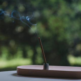 Incense stick in holder with rising smoke, wooden base
