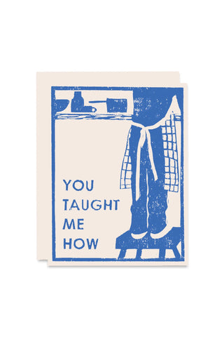 Blue letterpress-style card with text 'YOU TAUGHT ME HOW' and teacher desk figure