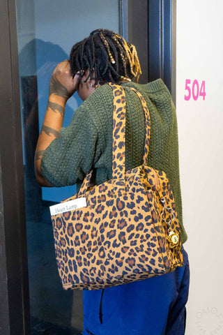 Person wearing a leopard print bag and green sweater, looking through a glass door