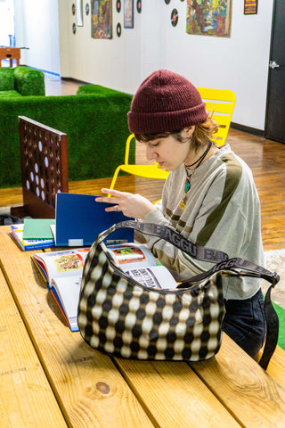 Person sitting at a table with a checkered bag, books, and a laptop in a casual setting.