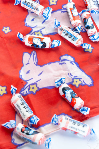 Candy rolls with cartoon characters on a red background with a white rabbit illustration.