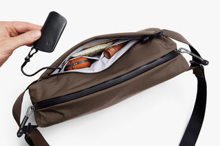 Brown crossbody bag with a hand holding a keychain for keys on a white background