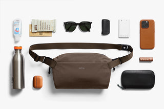 Brown sling bag with various items on a white background to show capacity of bag