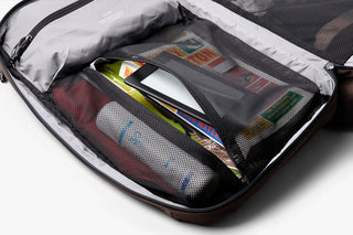 Open travel bag with compartments containing a tablet, book, and toiletries on a white background