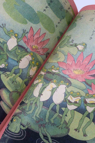 Open book page with whimsical frog figures and pink lotus flowers on pale background