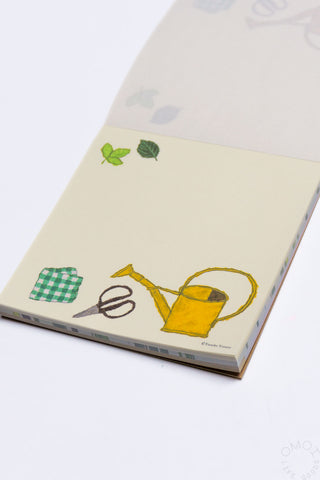 Memo pad with illustrations of a watering can, scissors, and leaves on a white background