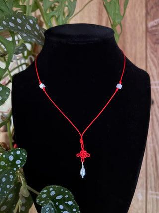 Red knot necklace with a pearl pendant on a black mannequin against a wooden background