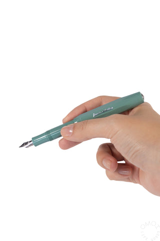 A hand holding a sage green fountain pen with a silver nib against a solid white background.