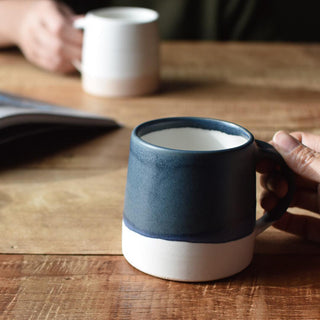 Person holding a blue and white ceramic mug on a wooden table
