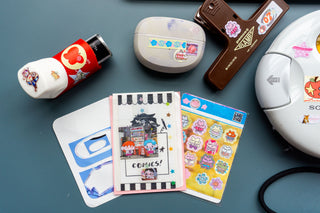 Collection of stickers sheets, earbuds, an inhaler, and a clamp decorated with stickers on a blue background