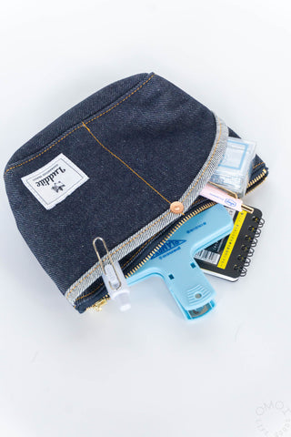 Small denim Luddite pouch on its side with blue clamp and pens on a white background