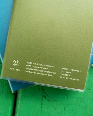 A close-up of a green planner cover showing printed text including '27' and quote 'NEVER PUT OFF TILL TOMORROW'...
