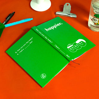 green journal on an orange surface with stationery items.