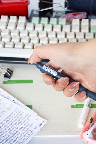 Hand holding OMOI Zento pen on a desk with a keyboard and planner