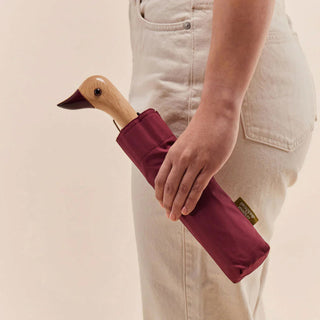 Person holding a maroon umbrella with a wooden handle against a beige background