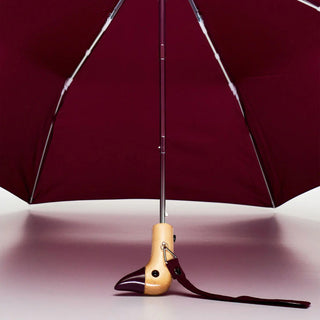 Maroon umbrella with wooden handle and strap on a light background