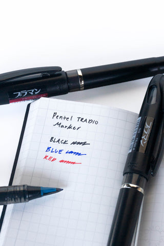 Black, blue, and red ink markers with pointed tips on a notebook.