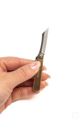 Mini pocket knife held in hand, vertical blade extended from brass handle