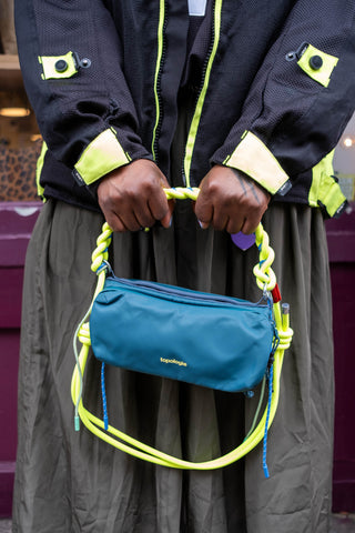 Person wearing a black jacket with yellow accents holding a blue bag with colorful straps.
