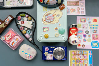 Assortment of sticker sheets and a camera, earbuds, and toolbox decorated with stickers on a blue backround